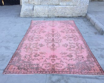 May include: A vintage rug in pink and brown with a floral pattern. The rug has a faded look and is made of wool.