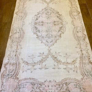 May include: A vintage-style rug with a light beige background and a delicate floral pattern in shades of pink and brown. The rug has a distressed look, giving it a unique and charming character.