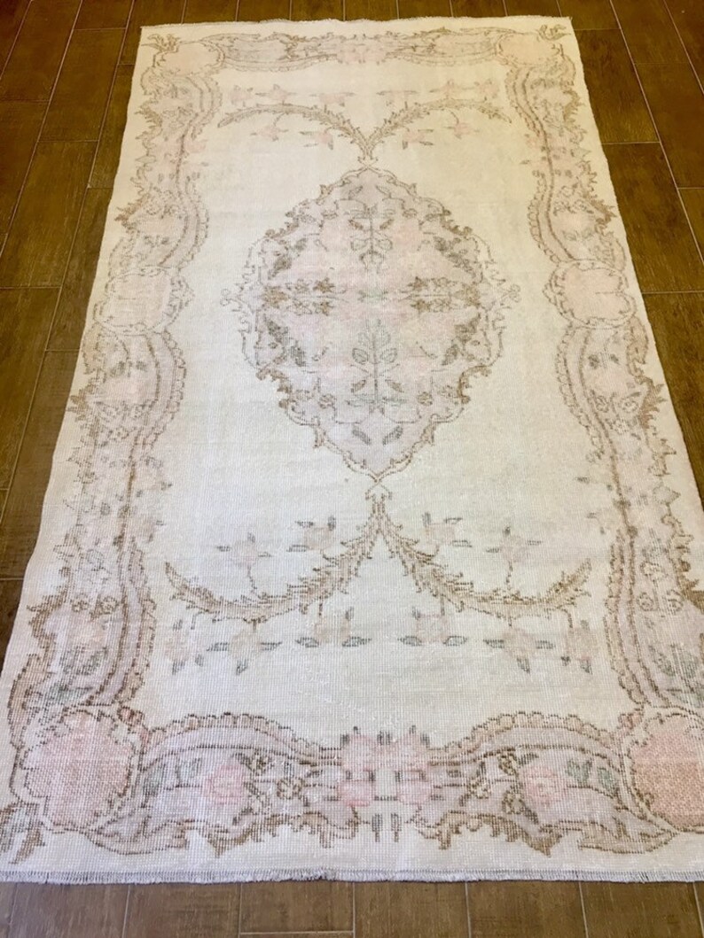 May include: A vintage-style rug with a light beige background and a delicate floral pattern in shades of pink and brown. The rug has a distressed look, giving it a unique and charming character.
