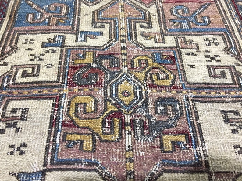 May include: Close-up of a vintage rug with a detailed geometric pattern in shades of red, blue, yellow, and beige. The rug has a worn and faded look, suggesting it is antique.