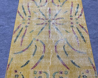 May include: A vintage rug with a yellow background and a pattern of green, pink, and white lines and shapes.