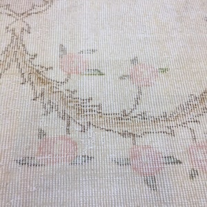May include: Close-up of a white rug with a subtle floral pattern in shades of pink and brown. The rug has a woven texture and a delicate design.