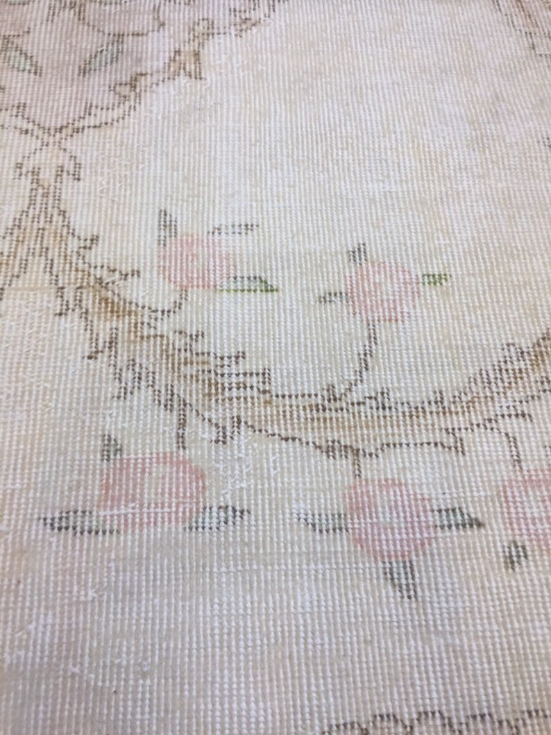 May include: Close-up of a white rug with a subtle floral pattern in shades of pink and brown. The rug has a woven texture and a delicate design.