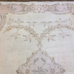 May include: A vintage cream-colored rug with a delicate floral pattern in shades of pink and brown. The rug has a distressed look, giving it a unique and charming character.