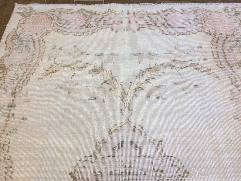 May include: A vintage cream-colored rug with a delicate floral pattern in shades of pink and brown. The rug has a distressed look, giving it a unique and charming character.