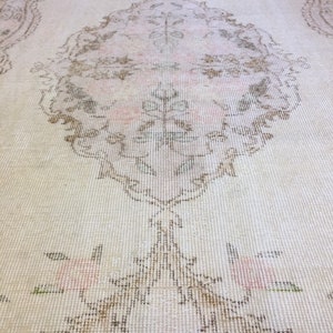 May include: A vintage cream-colored rug with a delicate floral pattern in shades of brown, pink, and green. The rug has a distressed look and a subtle sheen.