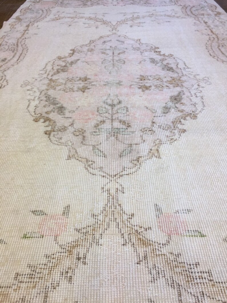 May include: A vintage cream-colored rug with a delicate floral pattern in shades of brown, pink, and green. The rug has a distressed look and a subtle sheen.