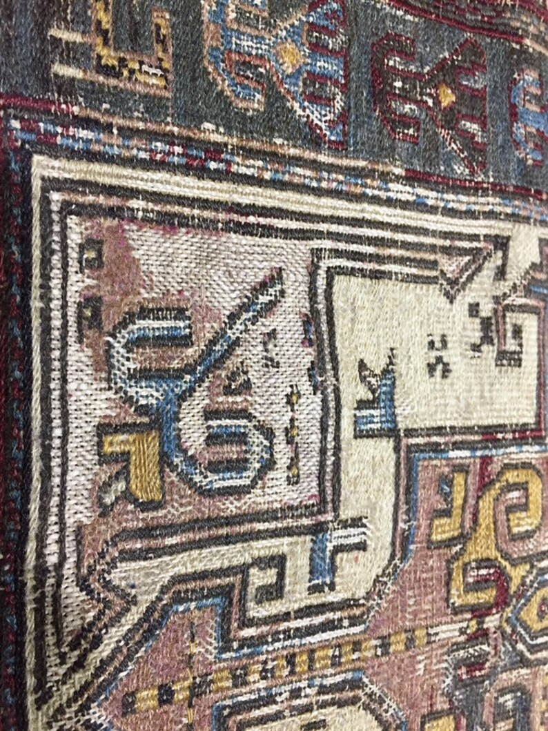 May include: Close-up of a vintage rug with intricate patterns in shades of blue, red, brown, and gold. The rug has a worn and faded appearance, suggesting it is an antique.