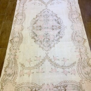 May include: A white vintage rug with a delicate floral pattern in shades of pink and brown. The rug has a distressed look and a subtle sheen.