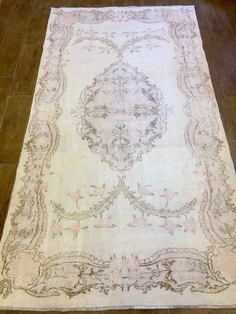 May include: A white vintage rug with a delicate floral pattern in shades of pink and brown. The rug has a distressed look and a subtle sheen.