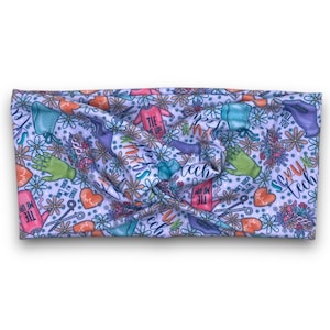 May include: A white headband with a colorful floral and medical-themed pattern. The design includes images of scrubs, gloves, scissors, and the text "Tie Me Up!" and "Sexy Tech". The headband is made of a soft, stretchy material.