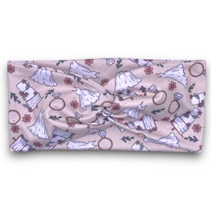 May include: A pink and white headband with a repeating pattern of wedding dresses, rings, and cakes.
