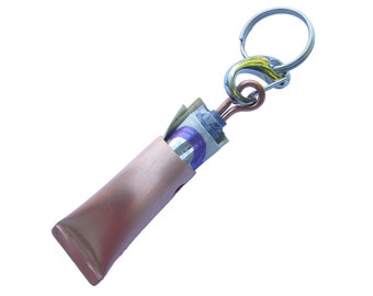 May include: A pink metal keychain with a silver ring and a copper hook. A rolled up bill of money is tucked inside the keychain.