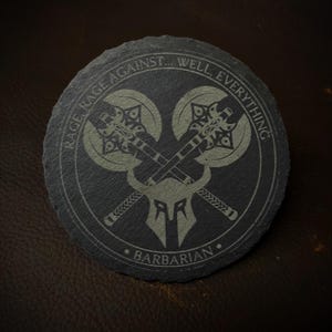 以下が含まれることがあります： グレーのデザインが施された、丸い黒いスレートコースター。デザインは、中央に角のあるヘルメットをつけた2つの交差した斧。デザインの周りに「RAGE AGAINST... WELL, EVERYTHING. BARBARIAN.」というテキストが刻まれています。