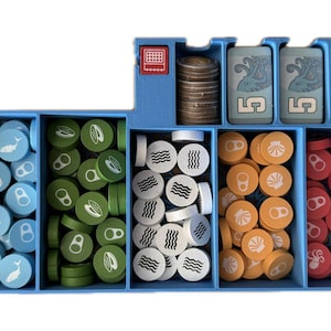 May include: A blue plastic organizer with six compartments. The compartments contain various colored tokens with different symbols, including fish, waves, seashells, and octopus. There are also two blue cards with the number "5" on them and a red card with the number "10" on it.