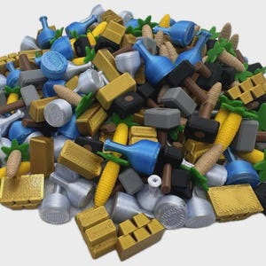 Op de afbeelding: Een stapel diverse miniatuur spelstukken in verschillende kleuren. De stukken omvatten blauwe flessen, goudstaven, grijze hamers, gele maïs en groene palmbomen. Andere stukken zijn zilveren containers en bruine houten stukken.
