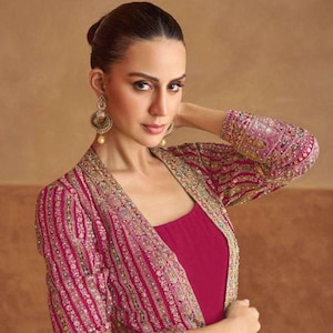 May include: A vibrant magenta sleeveless dress paired with a matching long-sleeved open jacket. The jacket features intricate gold embroidery, sequins, and beadwork in vertical patterns. The dress has a simple square neckline and a solid color.