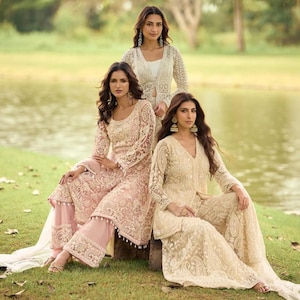 May include: Three outfits featuring long-sleeved, knee-length tunics with intricate white and pale pink floral embroidery. The garments include matching wide-leg trousers with lace detailing and scalloped hems, showcasing delicate craftsmanship.