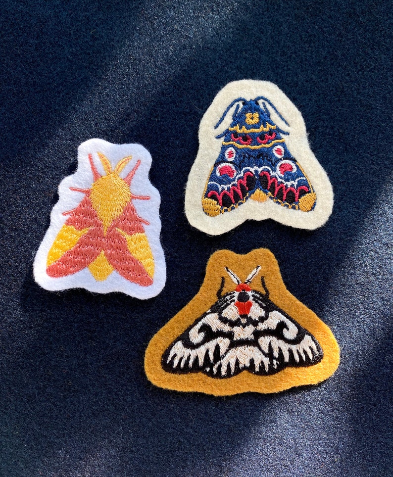 May include: Three embroidered felt moth patches. One is yellow and red, one is blue and red, and one is black and white on a yellow background.