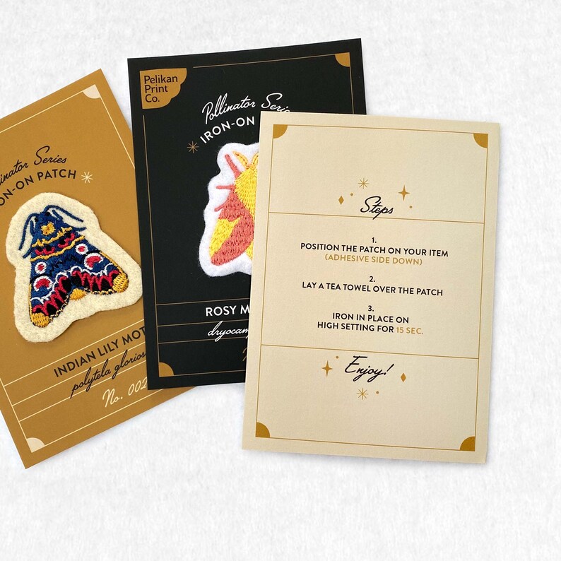 May include: Three iron-on patches featuring colorful embroidered moths. The patches are on cards with instructions for applying them. The instructions include "Position the patch on your item (adhesive side down)", "Lay a tea towel over the patch", and "Iron in place on high setting for 15 sec.". The text also includes "Pollinator Series", "Iron-On", "Rosy Maple Moth", "Dryocampa rubicunda", "Indian Lily Moth", "Polytela gloriosa", and "Enjoy!"