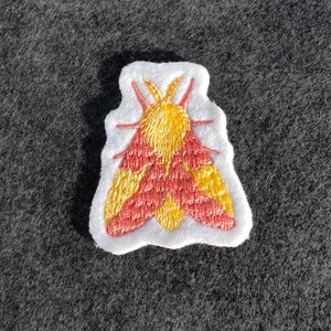 May include: A red and yellow embroidered moth patch on a white background.