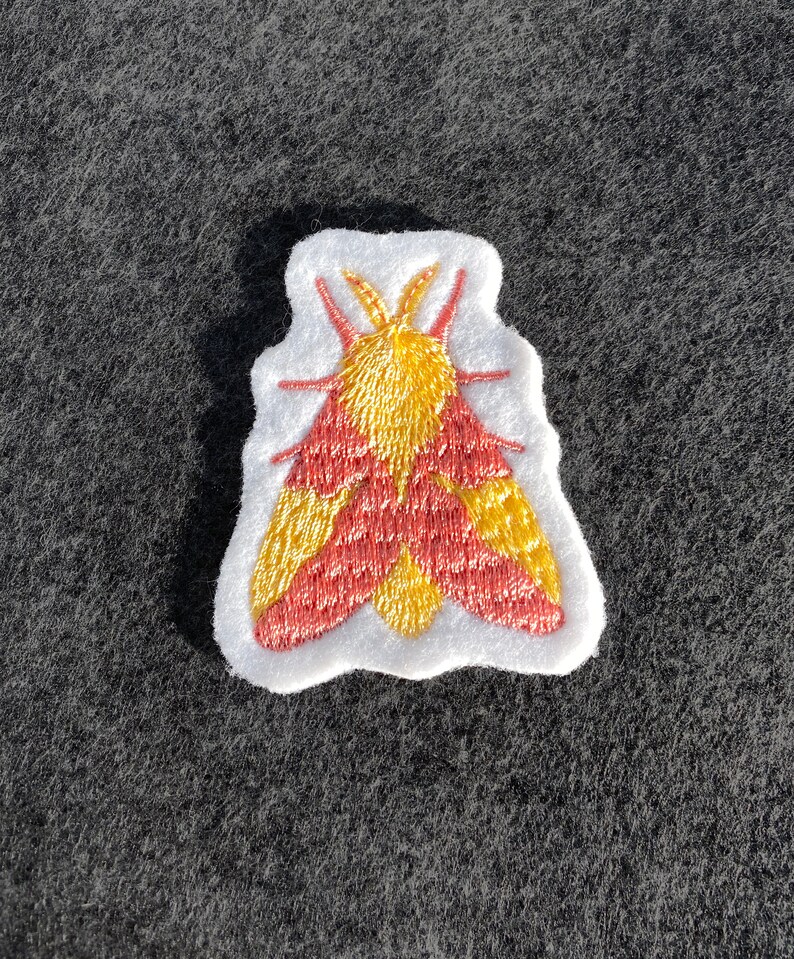 May include: A red and yellow embroidered moth patch on a white background.