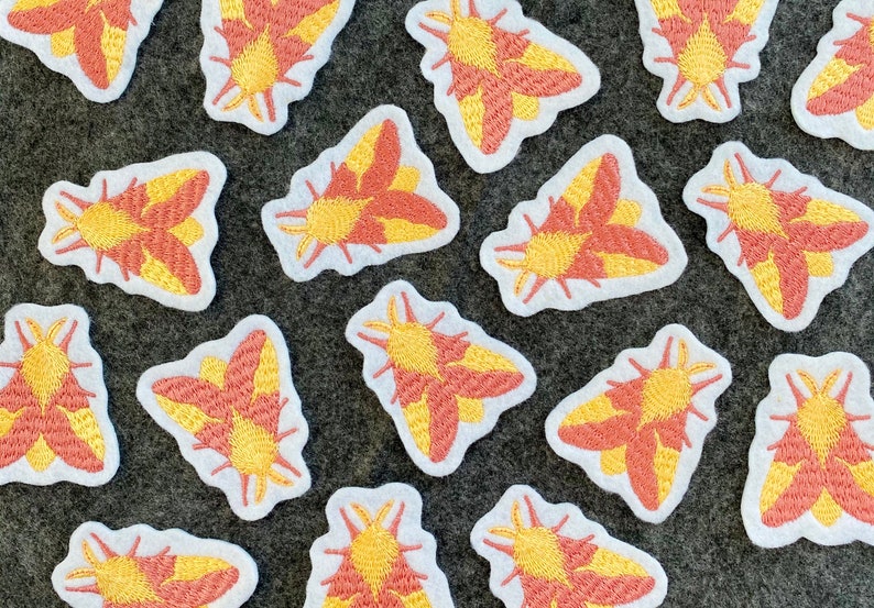 May include: A collection of 15 embroidered iron-on patches featuring a moth design in shades of pink and yellow. The patches are on a white background.