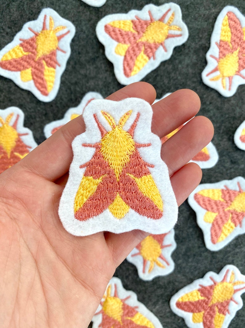 May include: A set of embroidered iron-on patches featuring a yellow and pink moth design. The patches are perfect for adding a touch of whimsy to clothing, bags, or other fabric items.