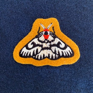 May include: A yellow felt patch with an embroidered black and white moth with red accents.