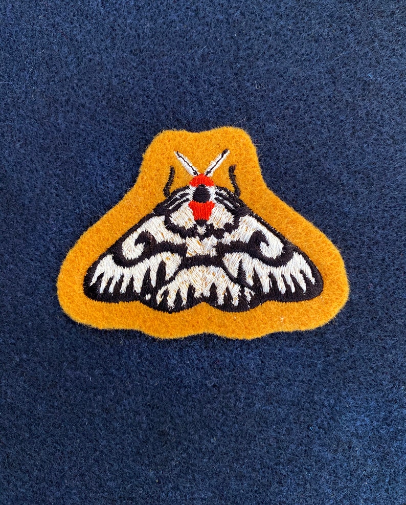May include: A yellow felt patch with an embroidered black and white moth with red accents.