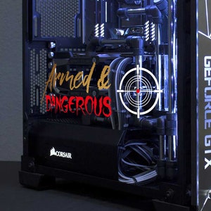 Op de afbeelding: Een zwarte en zilveren computertoren met interne componenten verlicht door blauwe lichten. De woorden "Armed & Dangerous" zijn zichtbaar in het rood, samen met een vizier. Het zijpaneel heeft een geometrisch ontwerp en de tekst "GEFORCE GTX".