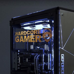 Op de afbeelding: Een op maat gemaakte gaming-pc met een zwarte behuizing en een transparant zijpaneel. De behuizing heeft blauwe interne verlichting en de tekst "HARDCORE GAMER" in goud. Het zijpaneel heeft een geometrisch ontwerp met witte accenten en de tekst "GEFORCE GTX".