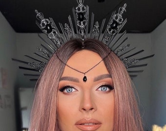 May include: A woman with pink hair is wearing a silver and black crown with black jewels. The crown is a halo style with spikes radiating out from the center.