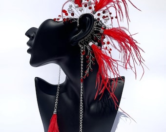 May include: A striking red feather and bead headpiece and ear cuff. The headpiece features red feathers, red beads, and silver wire accents. The ear cuff has a chain with a red feather tassel. The headpiece is displayed on a black mannequin head.
