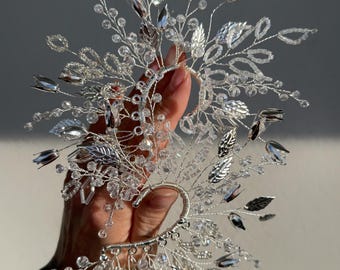May include: A silver-toned ear cuff featuring an intricate wire-wrapped design adorned with clear crystal beads and metallic leaf-shaped accents. The structure branches outward with delicate wire stems, creating a botanical-inspired accessory.