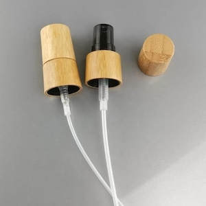 May include: Two spray pump mechanisms featuring light brown wooden collars and clear plastic dip tubes, accompanied by a separate matching cylindrical wooden cap. The pump heads are black plastic, and the collars have a visible wood grain texture.