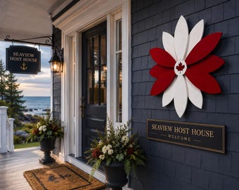 May include: A dark blue exterior wall features a large red and white flower-shaped wall decor with a central maple leaf emblem. Below it, a rectangular black sign displays the text SEAVIEW HOST HOUSE WELCOME in gold lettering.