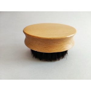 May include: A round wooden brush with black bristles. The brush has a natural wood finish and is designed for grooming.