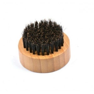 May include: A round, wooden brush with black bristles. The brush is made of bamboo and has a natural wood finish.