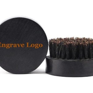 May include: Black wooden brush with natural bristles. The brush has a round shape and a flat base. The base has the text "Engrave Logo" printed on it.