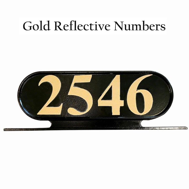 Op de afbeelding: Zwart ovaalvormig huisnummerbord met gouden reflecterende cijfers 2546. Het bord is gemonteerd op een zwarte metalen beugel.