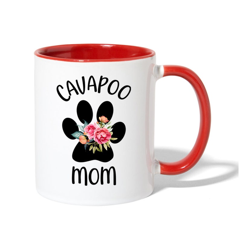 May include: White ceramic mug with a red interior and handle. The mug features a black paw print design with pink and peach flowers, and the words "CAVAPOO MOM" in black lettering.