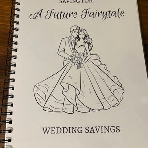 Könnte beinhalten: Ein spiralgebundenes Notizbuch mit dem Text "Saving For A Future Fairytale" und "Wedding Savings". Das Cover zeigt eine Schwarz-Weiß-Illustration eines Brautpaares. Das Notizbuch liegt auf einer dunklen Holzoberfläche.