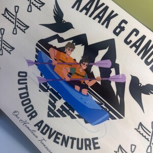 May include: A white rectangular sign with the words "KAYAK & CANOE OUTDOOR ADVENTURE" in black. The sign features a blue kayak with two people paddling, black mountain silhouettes, and bird illustrations. The text "Our Hometown Treasures" is also included.
