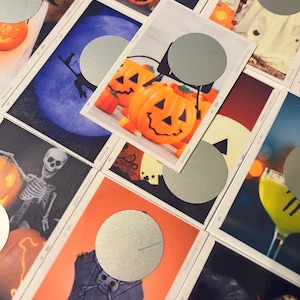 以下が含まれることがあります： ハロウィンをテーマにしたスクラッチカードのセット。かぼちゃ、骸骨、幽霊など、さまざまな画像が描かれています。各カードには、スクラッチして隠された画像を明らかにできる銀色の円があります。