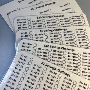 Puede incluir: Varias tarjetas blancas de desafío de ahorro con texto negro y círculos para marcar el progreso. Las tarjetas están etiquetadas con cantidades como 100 €, 50 €, 20 €, 10 € y 1 €, cada una con objetivos de ahorro correspondientes.