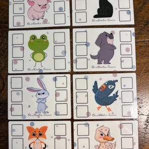 以下が含まれることがあります： 怒った表情の漫画の動物が描かれた8枚の白いカードのセット。 各カードには、豚、猫、カエル、犬、ウサギ、鳥、キツネ、アヒルの異なる動物が描かれています。 各カードには正方形のグリッドと「Our Hometown Treasures」のテキストがあります。