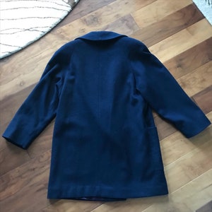 Pu&ograve; includere: Un cappotto di lana blu scuro con un colletto classico e maniche lunghe. Il cappotto ha una chiusura con un solo bottone e due tasche.