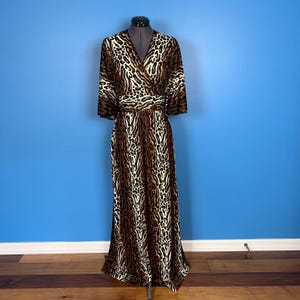 May include: A long, brown and white leopard print maxi dress with a V-neckline and a wrap style bodice. The dress has a belt at the waist and 3/4 sleeves.