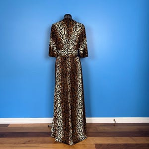 Puede incluir: Un vestido maxi largo de estampado de leopardo marr&oacute;n y blanco con cintur&oacute;n. El vestido tiene cuello en V y mangas cortas.